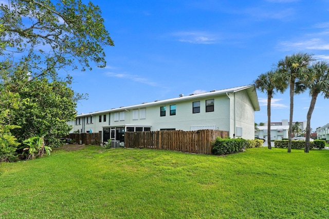 back of property with a lawn, stucco siding, fence, and central air condition unit