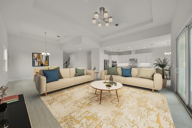 living room with a healthy amount of sunlight, a notable chandelier, a raised ceiling, and light wood-type flooring