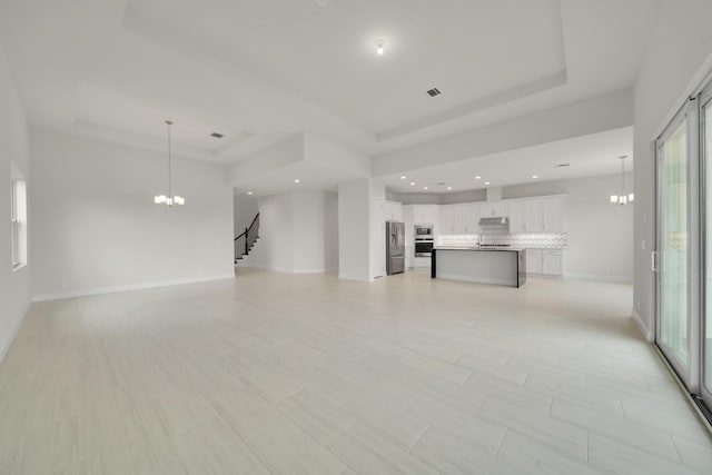 unfurnished living room featuring a healthy amount of sunlight, a chandelier, and a tray ceiling