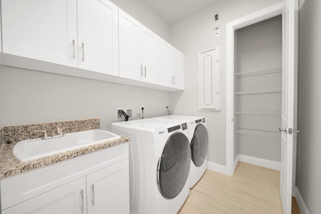 clothes washing area featuring sink, light wood-type flooring, washer and clothes dryer, cabinets, and electric panel