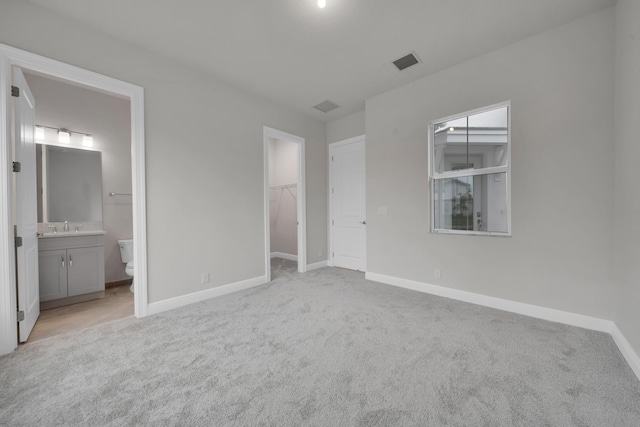 unfurnished bedroom featuring connected bathroom, light carpet, a closet, and a spacious closet