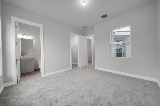 unfurnished bedroom featuring a spacious closet, ensuite bathroom, a closet, and light colored carpet