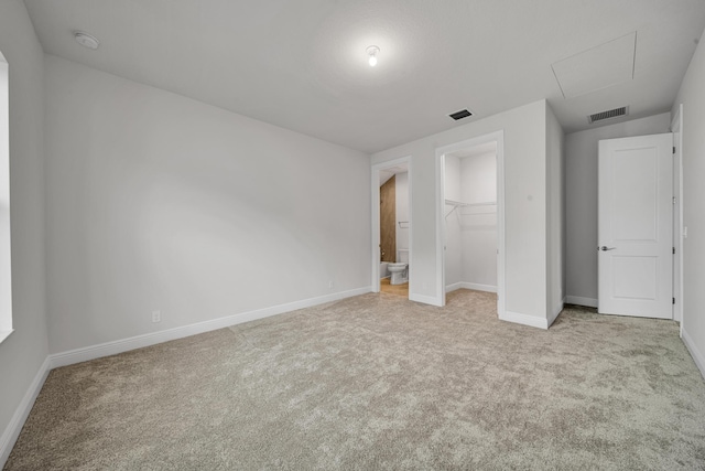 unfurnished bedroom featuring a spacious closet, a closet, and light colored carpet