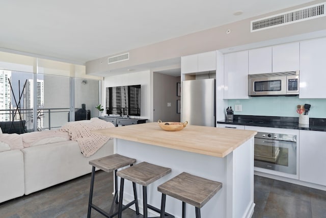 kitchen featuring white cabinetry, butcher block countertops, stainless steel appliances, and a breakfast bar area