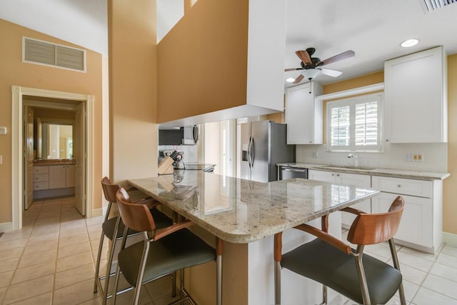 kitchen with white cabinets, a breakfast bar, kitchen peninsula, and light tile patterned floors