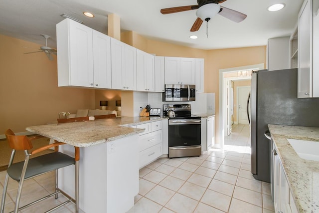 kitchen with a kitchen breakfast bar, light stone counters, kitchen peninsula, white cabinets, and appliances with stainless steel finishes