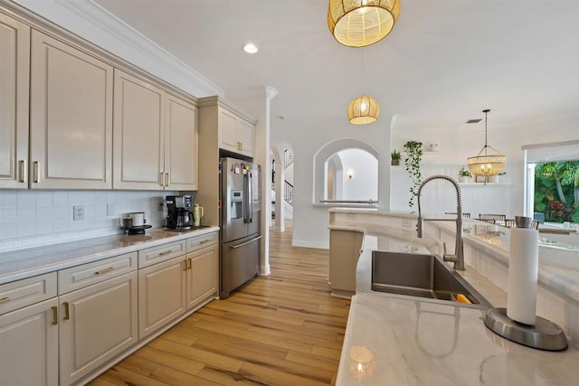 kitchen with stainless steel refrigerator with ice dispenser, crown molding, light stone countertops, pendant lighting, and light hardwood / wood-style floors