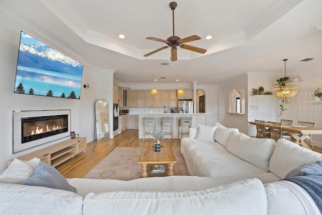 living room featuring crown molding, a tray ceiling, light wood-type flooring, and ceiling fan