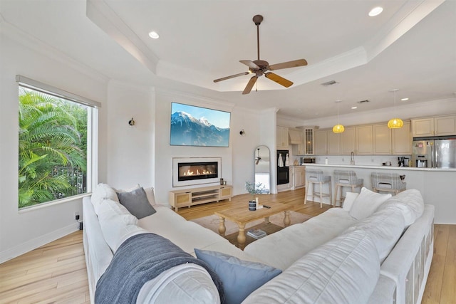 living room with crown molding, light hardwood / wood-style flooring, a tray ceiling, and ceiling fan