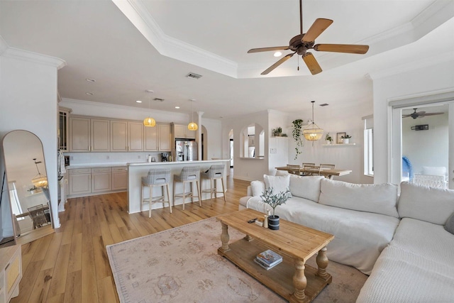 living room featuring light hardwood / wood-style flooring, ornamental molding, a tray ceiling, and ceiling fan