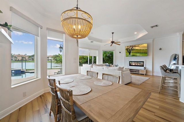 dining space with light hardwood / wood-style floors, ceiling fan, a water view, and a raised ceiling