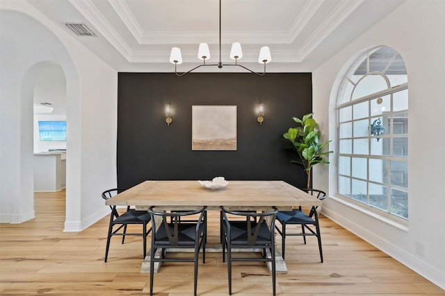 dining space featuring ornamental molding, light wood-type flooring, and a raised ceiling