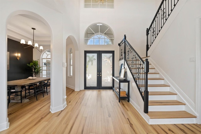 entryway featuring a notable chandelier, wood-type flooring, ornamental molding, a high ceiling, and french doors