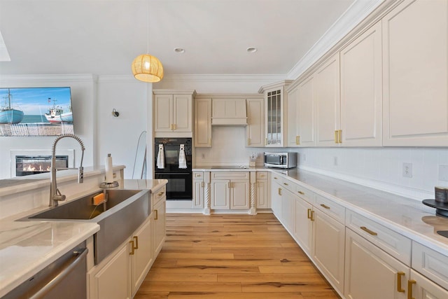 kitchen with sink, black appliances, crown molding, decorative light fixtures, and light hardwood / wood-style floors