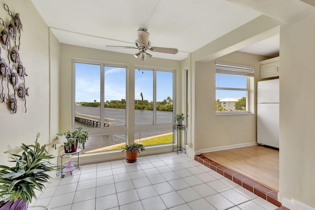 unfurnished sunroom featuring a water view, ceiling fan, and a wealth of natural light