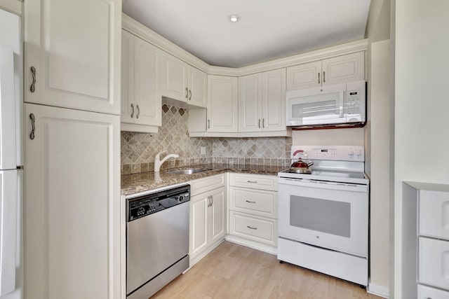 kitchen with white appliances, backsplash, sink, white cabinets, and light hardwood / wood-style floors