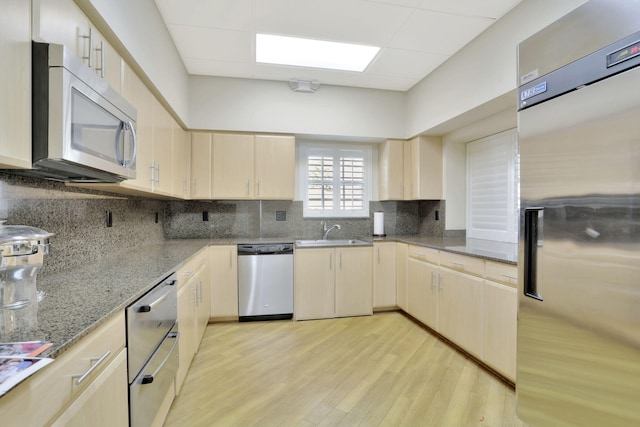 kitchen with tasteful backsplash, appliances with stainless steel finishes, light wood-type flooring, sink, and light stone counters