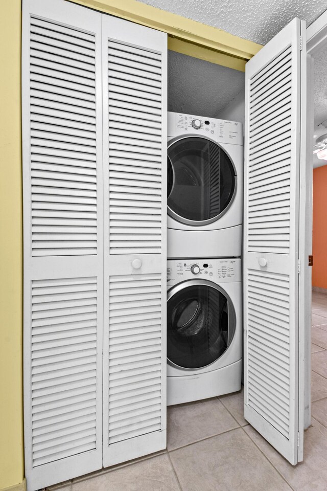 washroom featuring stacked washer and dryer, water heater, a textured ceiling, and light tile patterned flooring