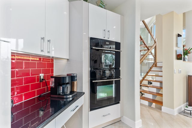 kitchen with decorative backsplash, white cabinetry, black double oven, and light tile patterned floors