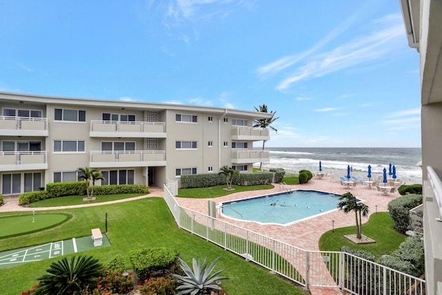 view of swimming pool featuring a lawn, a patio, a water view, and a beach view