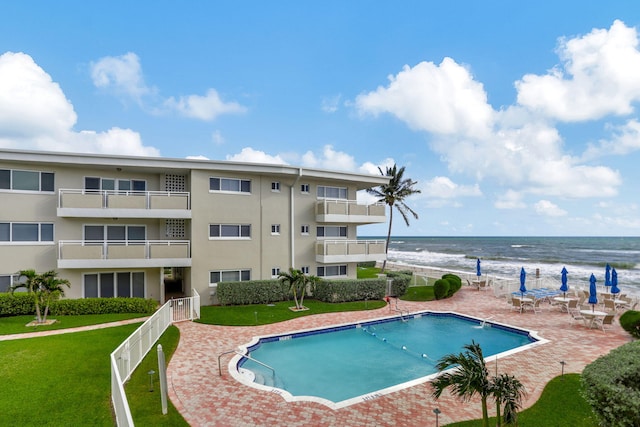 view of swimming pool with a yard, a beach view, a water view, and a patio area