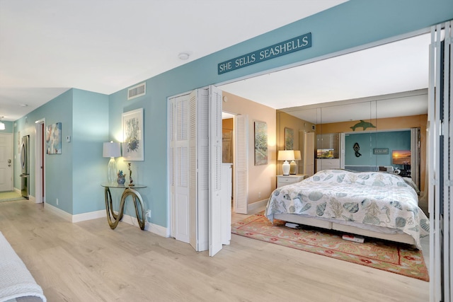 bedroom with light hardwood / wood-style floors, stainless steel fridge, and two closets