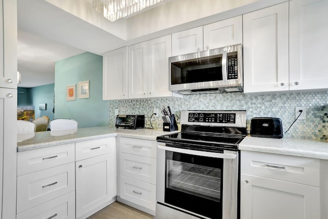 kitchen featuring white cabinets, stainless steel appliances, backsplash, and light stone countertops