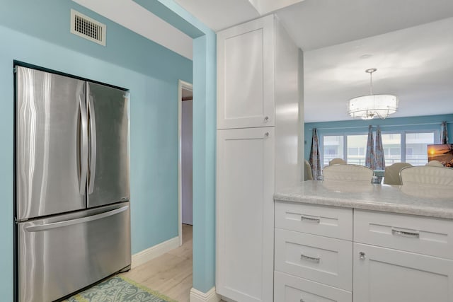 kitchen with white cabinets, stainless steel fridge, pendant lighting, and light hardwood / wood-style flooring