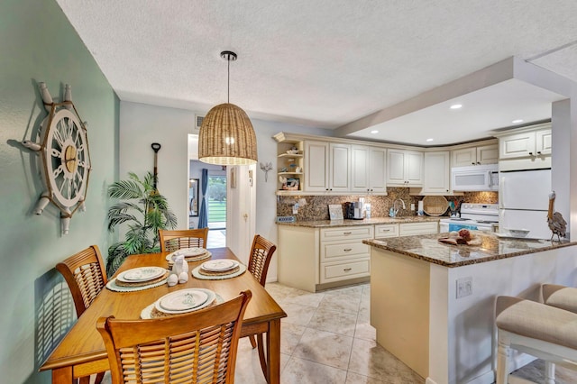 kitchen featuring hanging light fixtures, kitchen peninsula, dark stone counters, sink, and white appliances