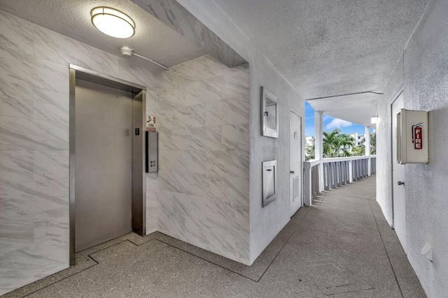 hall featuring a textured ceiling and elevator