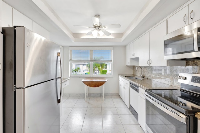 kitchen featuring sink, light tile patterned floors, a tray ceiling, white cabinets, and appliances with stainless steel finishes