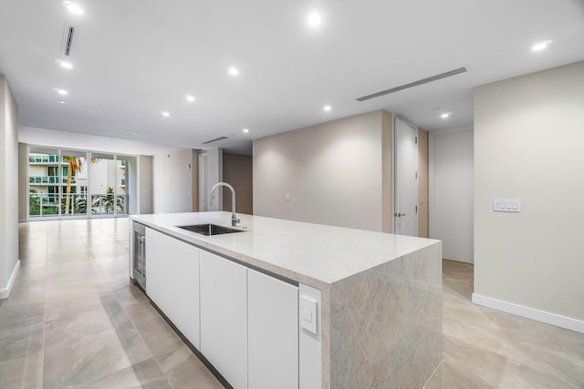 kitchen with white cabinetry, sink, and a kitchen island with sink