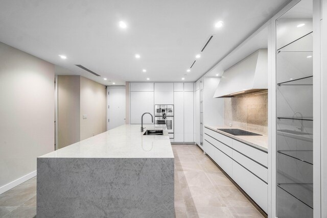 kitchen featuring sink, premium range hood, white cabinetry, backsplash, and a spacious island