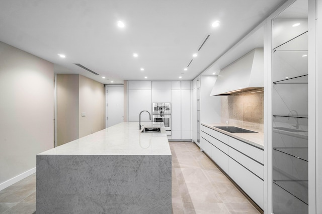 kitchen featuring sink, white cabinetry, decorative backsplash, custom exhaust hood, and a large island with sink