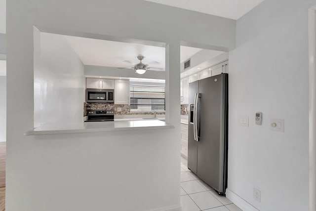 kitchen with decorative backsplash, kitchen peninsula, stainless steel appliances, light tile patterned floors, and white cabinetry