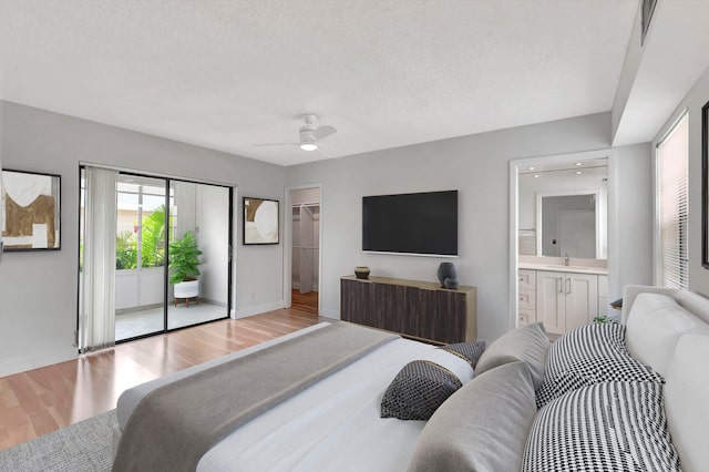 bedroom with ceiling fan, a textured ceiling, light hardwood / wood-style floors, and ensuite bath