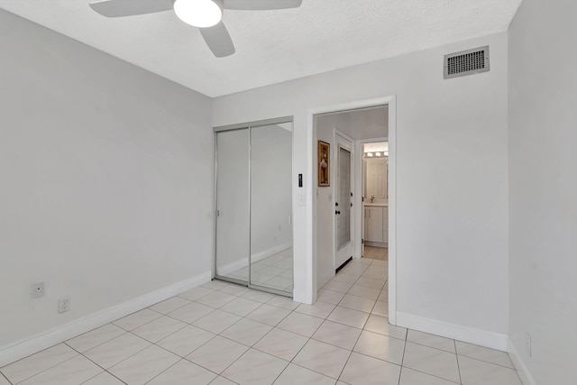 unfurnished bedroom featuring a closet, a textured ceiling, light tile patterned floors, and ceiling fan