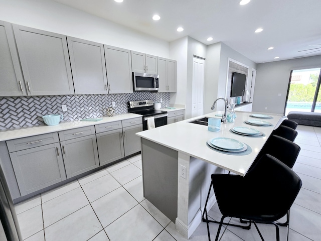 kitchen with gray cabinetry, a center island with sink, a kitchen breakfast bar, sink, and stainless steel appliances