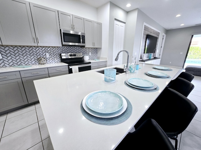 kitchen featuring a breakfast bar, stainless steel appliances, gray cabinets, and sink