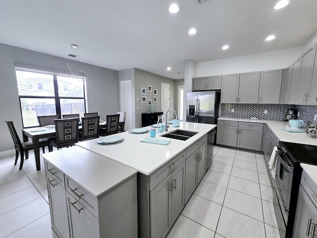 kitchen featuring gray cabinetry, sink, tasteful backsplash, a kitchen island with sink, and appliances with stainless steel finishes