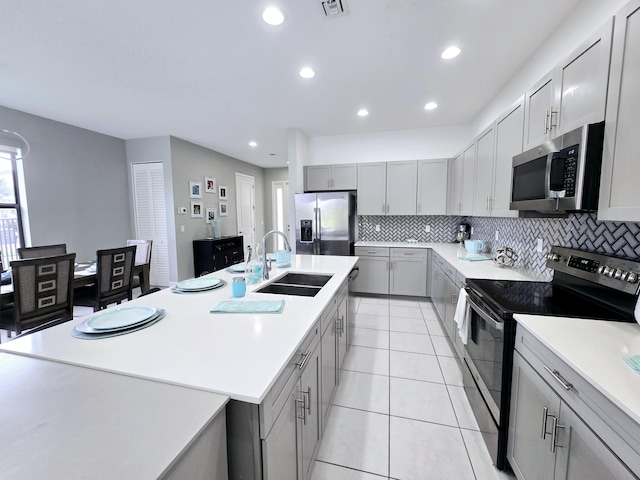 kitchen with decorative backsplash, stainless steel appliances, sink, a center island with sink, and gray cabinets