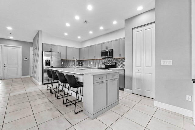 kitchen with sink, a kitchen island with sink, stainless steel appliances, decorative backsplash, and a breakfast bar