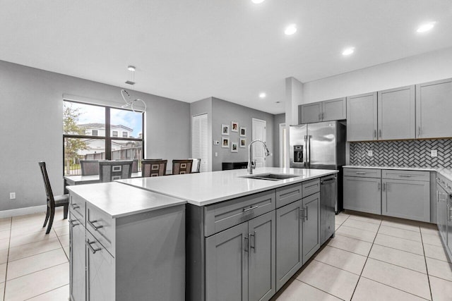 kitchen featuring sink, stainless steel appliances, gray cabinets, and an island with sink