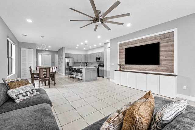 living room featuring ceiling fan with notable chandelier, light tile patterned flooring, and a textured ceiling