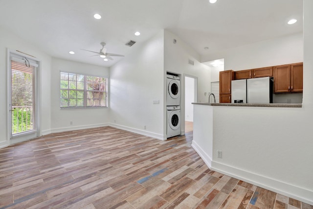 unfurnished living room with light hardwood / wood-style floors, stacked washer / dryer, lofted ceiling, and ceiling fan