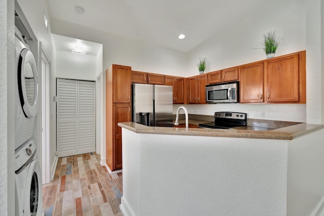 kitchen with stacked washer and clothes dryer, sink, light hardwood / wood-style flooring, kitchen peninsula, and stainless steel appliances