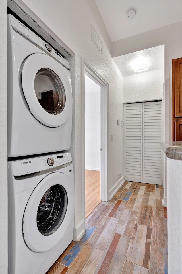 clothes washing area featuring light wood-type flooring and stacked washer and clothes dryer