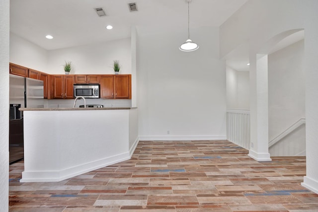 kitchen with kitchen peninsula, pendant lighting, stainless steel appliances, and light hardwood / wood-style flooring