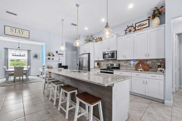 kitchen with white cabinetry, decorative light fixtures, stainless steel appliances, and an island with sink