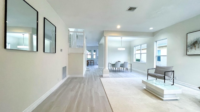 hallway with decorative columns, light hardwood / wood-style flooring, and plenty of natural light